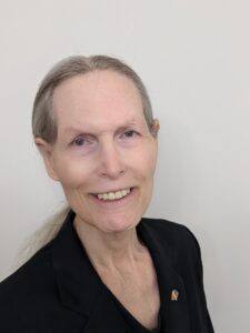 Portrait photo of Marsha, smiling while wearing a dark suit with her hair in a low ponytail, 2022. Photograph courtesy of Marsha Botzer. 