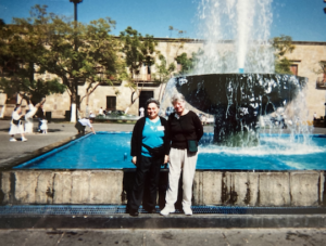 Harriet Miller and Monica Wehrle smile while posing together in front of a lively fountain in a city square on a Guadalajara Oats Tour. In Guadalajara, Mexico, 2001. Photo Courtesy of Harriet Miller and Monica Wehrle.