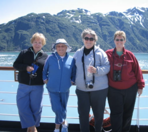 Monica Wehrle and Harriet Miller with  friends Sharon and Tina on an Alaskan Cruise, with some icy mountains in the background. Alaska, 2007. Photo Courtesy of Harriet Miller and Monica Wehrle.