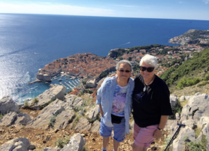 Harriet Miller and Monica Wehrle smile in sunglasses atop a seaside cliff overlooking a coastal city. In Croatia, 2015. Photo Courtesy of Harriet Miller and Monica Wehrle.