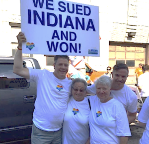 Harriet Miller and Monica Wehrle with other Indiana ACLU plaintiffs at Indianapolis Pride festival. Their group smiles while someone holds up the sign “We sued Indiana and WON!”  In Indianapolis, Indiana, 2015. Photo Courtesy of Harriet Miller and Monica Wehrle.