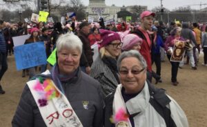 Monica Wehrle and Harriet Miller at the Women’s March on DC, smiling while holding up colorful protest posters  in Washington, D.C., 2017. Photo Courtesy of Harriet Miller and Monica Wehrle.