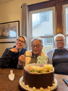 Harriet Miller and Monica Wehrle (center, Right) with daughter Sari Ohrn (L) smiling and eating a chocolate birthday cake. In Fort Wayne, Indiana, 2025. Photo Courtesy of Harriet Miller and Monica Wehrle.
